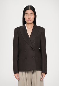 Blazer marrón de doble botonadura con solapas en pico, dos bolsillos frontales y seis botones. Textura suave con ajuste estructurado. Diseño a medida.