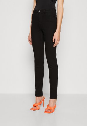 Black skinny jeans with a high waist, featuring a front button closure. Paired with orange strappy high-heeled shoes. Smooth texture.