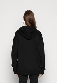 Svart hoodie med avslappnad passform, dragsko i huvan, ribbade muddar och fåll, tillverkad av mjukt tyg, med en enkel design utan synliga logotyper.