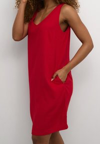 Rotes ärmelloses Kleid mit V-Ausschnitt, aus weichem Stoff gefertigt, mit einer Seitentasche und einem lockeren Schnitt, der oberhalb des Knies endet.
