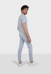 T-shirt in cotone grigio e pantaloni jogger abbinati con un design aderente, accompagnati da scarpe da ginnastica bianche, catturato di lato.