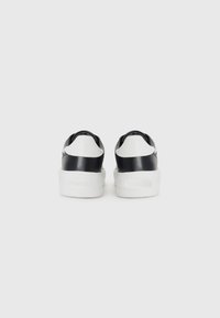 Zwart-witte sneakers met een gladde leren afwerking, een stevige witte zool en zwarte accenten bij de hiel en zijkanten. Merlogo zichtbaar.