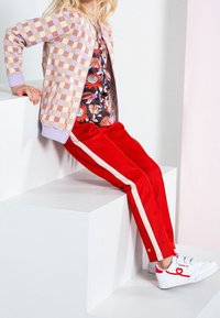Pasiakowane czerwone spodnie dresowe, czarna bluzka w kwiaty oraz jasna kardigan w kratkę. Białe trampki z czerwonym detalem w kształcie serca, siedząca na platformie.