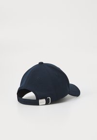 Sötétkék baseball sapka struktúrált anyagból, ívelt napellenzővel és állítható pánttal, amelyen fémes logó dísszel van ellátva.