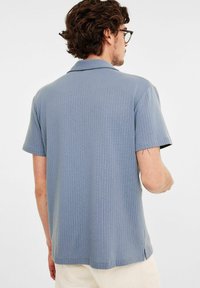 Korte mouwen, blauwe polo met een gestructureerd patroon en een open kraag. De zoom heeft zijsplitten, wat extra detail toevoegt aan het casual ontwerp.