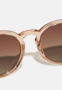 Brown-tinted sunglasses with a clear, glossy plastic frame, rounded lenses, and a smooth, wavy bridge connecting the lenses.