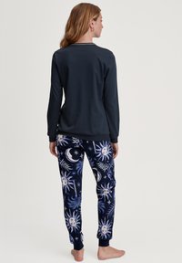 Marineblauw langmouwtop gecombineerd met blauwgepatenteerde broek met hemelse ontwerpen, waaronder zon- en maanmotieven, gemaakt van zachte stof.