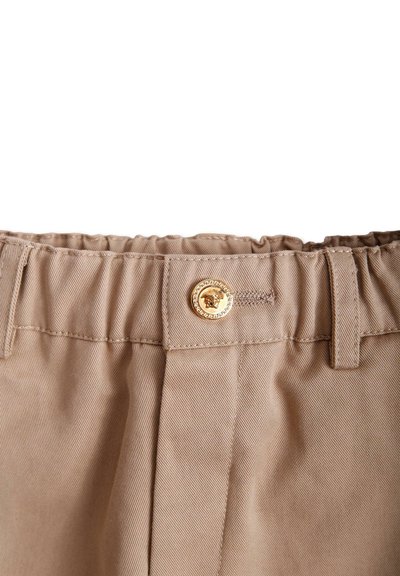 Beżowe spodnie z teksturowanej tkaniny, z elastycznym pasem i zapięciem na złoty guzik z detalem w formie herbu lwa.