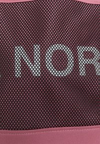 Top deportivo de malla con una combinación de colores negro y rosa. Presenta letras grandes que dicen "NORD", agujeros de ventilación en forma circular y una superficie texturizada.