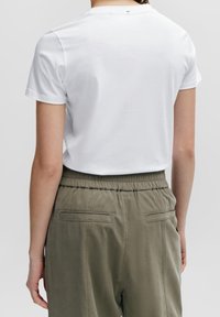 Vit bomullströja med korta ärmar, bakvy. Matchad med olivgröna byxor med elastisk midja som har två bakfickor och sid sömmar.