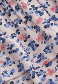 Blommönstrat tyg med blå, rosa och svarta blommor på en mjuk, ljusrosa bakgrund. Slät struktur med flödande fall.