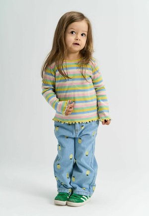 Multicolored striped long-sleeve shirt with ruffled hem, paired with light blue jeans featuring pineapple patterns, and green sneakers.