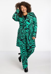 Groen en zwart gestreept pak met een lange jas en bijpassende broek. De stof is zacht en heeft een gedurfde tijgerstrepenpatroon.