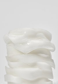 Pile de fines couches de tissu blanc translucide avec une texture douce et ondulée sur un fond clair uni.