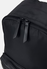 Černý batoh vyrobený z texturovaného nylonu, s dvojitým zipem a koženými táhlíky, a hladkým koženým akcentem na spodní straně.