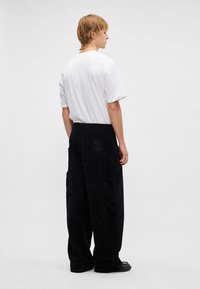 Fekete kordbársony bő szárú nadrág nagy zsebekkel és egy koponya mintás hátsó zsebbel. Egyszerű fehér pólóval párosítva.