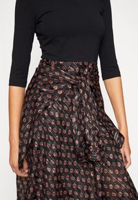 Spódnica w kwiaty z plisami, z czarnym tłem i wzorem w czerwono-białe kwiaty, przewiązana w talii pasującym materiałowym paskiem oraz o lekko opadającej strukturze.