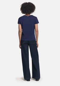 Camiseta de algodón azul marino con cuello redondo, mangas cortas y un pequeño detalle de logo en la parte posterior, combinada con pantalones vaqueros de pierna ancha de mezclilla oscura.