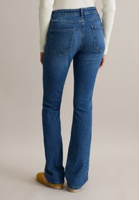 Ausgestellte Jeans aus Denim in Mittelblau mit glatter Textur. Verfügt über zwei Gesäßtaschen, einen mittelhohen Bund und minimale Nähdetails.