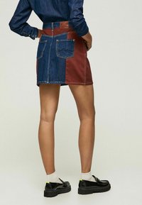 Jeansenkjol med en färgblockdesign med mörkblå och vinröda paneler, fem fickor och en brun läderlapp vid midjan.