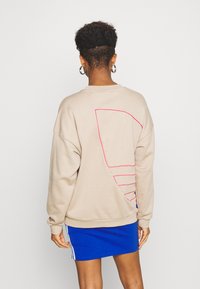 Beige mikina s růžovým geometrickým designem na zádech, s žebrovanými manžetami a lemem. Nosená přes modrou sukni s bílými pruhy.