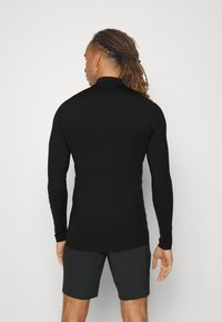 Black long-sleeve athletic top with a high collar, fitted design, smooth texture, and thumbholes, paired with dark shorts.