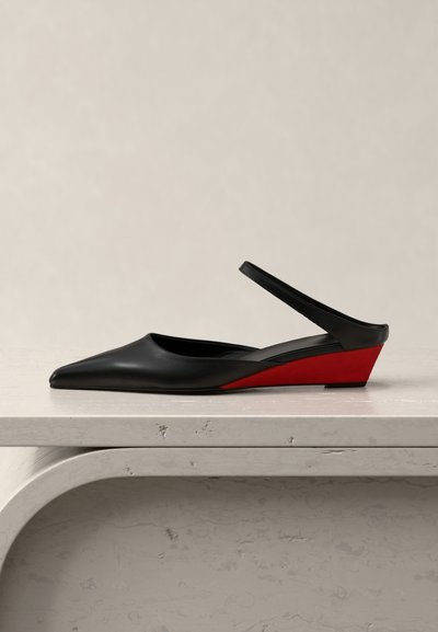 Μαύρο δερμάτινο παπούτσι slingback με μυτερή μύτη και χαμηλό κόκκινο τακούνι σε σφήνα, τοποθετημένο σε ανοιχτό μαρμάρινο φόντο με μπεζ φόντο.