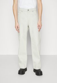 Pantalones de denim gris claro con un ajuste holgado, diseño de cinco bolsillos, cierre frontal con botón y tejido texturizado, acompañados de zapatos negros gruesos.