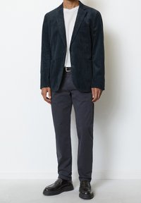 Blazer in corduroy blu navy con tasche a toppa, indossato su una t-shirt bianca e abbinato a pantaloni scuri e mocassini neri. Design testurizzato e strutturato.