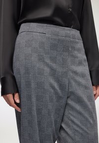 Zbliżenie na osobę w szarej kraciastej spódnicy i czarnej satynowej koszuli z długim rękawem z zapiętymi mankietami.