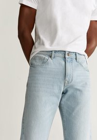 Vaqueros de denim azul claro con un corte clásico, que cuentan con un cierre de botón, bolsillos frontales y una textura ligeramente desgastada.