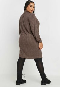 Brun ribbad klänning med hög krage och långa ärmar, kombinerad med svarta ankelstövlar och strumpbyxor, som visar en avslappnad passform och mjuk textur.