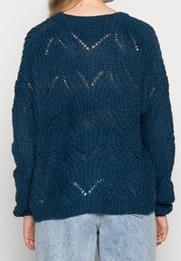 Stickad blå tröja med en lös, texturerad design och öppen väv, långa ärmar och en vid halsringning.