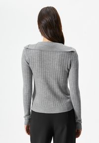 Maglioncino grigio a coste con collo posteriore e maniche lunghe, caratterizzato da un design aderente e un tessuto testurizzato. Indossato con pantaloni neri.