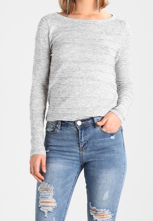 Light gray long-sleeve top with a ribbed texture, paired with distressed blue jeans featuring rip accents and a high waist.