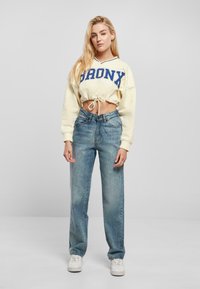 Light yellow cropped sweatshirt with "BRONX" in blue, paired with high-waisted, faded blue straight-leg jeans and white sneakers.