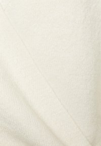 Krämfärgad stickad tyg med en mjuk textur, med en diagonal söm och ett subtilt ribbat mönster.