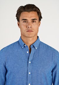 Camicia azzurro chiaro con bottoni, realizzata in tessuto strutturato; presenta un colletto e bottoni bianchi, con taglio dritto e maniche lunghe.