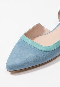 Niebieskie zamszowe buty płaskie z ostrym noskiem i jasnoniebieską lamówką wzdłuż górnej krawędzi. Gładka podszewka, minimalistyczny design.