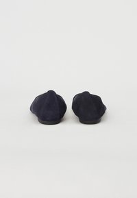 Ballerines en daim bleu marine avec une texture douce, un bout rond et un talon bas, présentant un design simple et sans embellissements visibles.