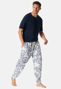 Herren-Hemden in Marineblau mit kurzen Ärmeln, kombiniert mit weißen Hosen mit blauen, kreisförmigen Mustern. Die Hose hat einen elastischen Bund und seitliche Taschen.