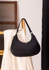 Czarna nylonowa torba na ramię o zakrzywionym kształcie, z akcentami w kolorze złotym i zamkiem błyskawicznym. Pasek jest regulowany i przymocowany na obu końcach.