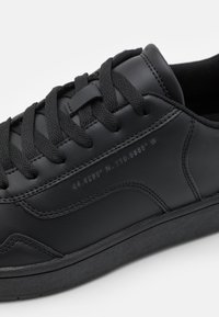 Black leather sneaker with flat black laces, minimal design, and embossed coordinates on the side. Textured surface with smooth accents.