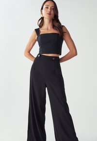 Czarny crop top o kwadratowym dekolcie i szerokich ramiączkach, zestawiony z czarnymi, wysokim stanem spodniami typu wide-leg z guzikami i gładkiego materiału.