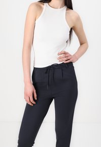 Vit ärmlös ribbad topp i kombination med mörknavy skräddade byxor med dragsko och sidofickor. Slät textur överlag.