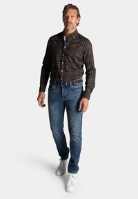 Bruine geblokte overhemd met blauwe accenten, gecombineerd met blauwe denim jeans en witte sneakers. Inclusief een blauwe gevlochten riem.