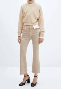 Pull encolure ras du cou beige, longueur courte, associé à un jean flare beige clair, ourlet brut, complété par des chaussures à talons carrés noirs brillants.