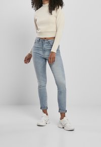 Suéter cropped color beige claro con mangas largas, combinado con jeans ajustados azul claro enrollados en los puños y zapatillas blancas.