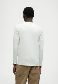 Long-sleeve, light gray t-shirt made of soft cotton. Round neckline with a smooth texture, paired with brown corduroy pants.