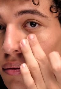 Primo piano di una persona che applica un prodotto sulla pelle intorno all'occhio. La pelle è liscia e ha una carnagione chiara. Le mani sono naturali e non curate.